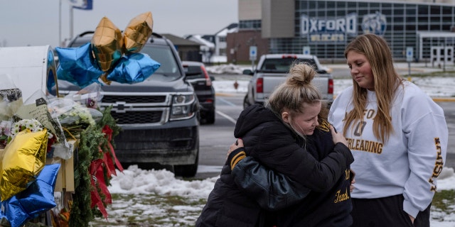 People embrace as they pay their respects at a memorial at Oxford High School, a day after a shooting that left four dead and eight injured, in Oxford, Michigan.