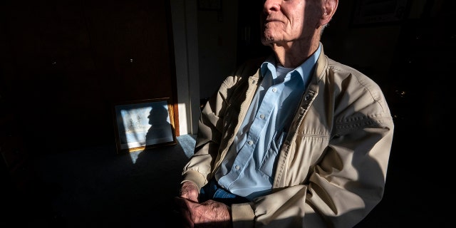 Pearl Harbor survivor and World War II Navy veteran David Russell, 101, poses for a photo along with a painting of the USS Oklahoma at his home on Monday, Nov. 22, 2021, in Albany, Ore. (AP Photo/Nathan Howard)