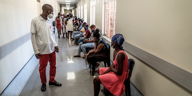 A hospital worker ensures people practice social distancing as they wait in line to get vaccinated against COVID-19 at the Lenasia South Hospital, near Johannesburg, South Africa, Wednesday, Dec. 1, 2021. Despite the global worry, doctors in South Africa are reporting patients with the omicron variant are suffering mostly mild symptoms so far. But they warn that it is early. 