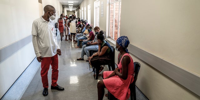 A hospital worker ensures people practice social distancing as they wait in line to get vaccinated against COVID-19 at the Lenasia South Hospital, near Johannesburg, South Africa, Wednesday, Dec. 1, 2021. Despite the global worry, doctors in South Africa are reporting patients with the omicron variant are suffering mostly mild symptoms so far. But they warn that it is early.