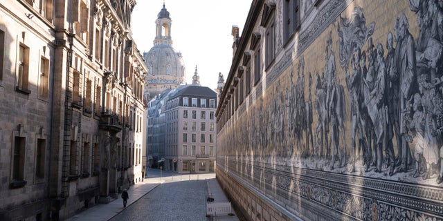 Un passant marche le long de l'Augustusstrasse vide à côté de la fresque « Fuerstenzug » devant la Frauenkirche à Dresde, en Allemagne, le jeudi 2 décembre 2021. Photo : Sebastian Kahnert/dpa via AP)