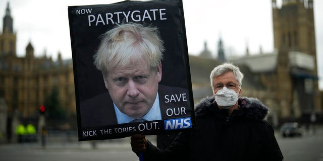 An anti-Tory protester holds a sign with a picture of UK Prime Minister Boris Johnson including the words "Now Partygate" against the backdrop by the Houses of Parliament, London, Wednesday, December 8, 2021. British Prime Minister Boris Johnson on Wednesday ordered an investigation and said he was "mad" after a leaked video showed senior members of its staff joking about hosting a Christmas party violating the lockdown.  (AP Photo / Matt Dunham)