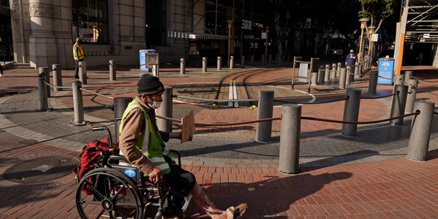 A man panhandling in a wheelchair, with open sores on his legs, makes his way past the Powell and Market Street cable car turnaround in San Francisco, Thursday, Dec. 2, 2021. (AP Photo/Eric Risberg)