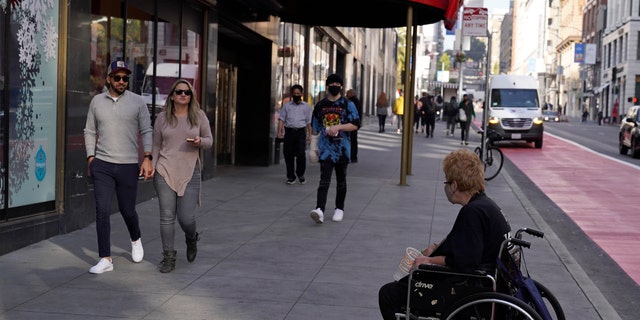 People walk past a female beggar in a wheelchair near Union Square in San Francisco on Thursday, December 2, 2021. (AP Photo / Eric Risberg)