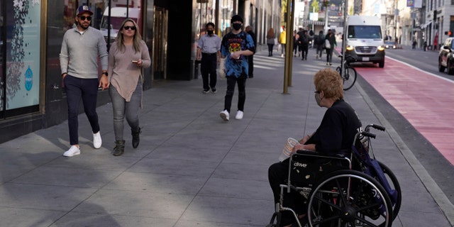 People pass by a woman in a wheelchair panhandling near Union Square in San Francisco, Thursday, Dec. 2, 2021. (AP Photo/Eric Risberg)