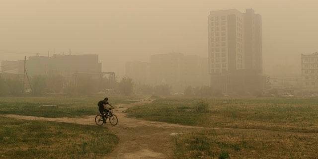 A man rides his bicycle through smoke from a forest fire covers Yakutsk, the capital of the republic of Sakha also known as Yakutia, Russia Far East, Russia, Thursday, Aug. 12, 2021. (AP Photo/Ivan Nikiforov, File)