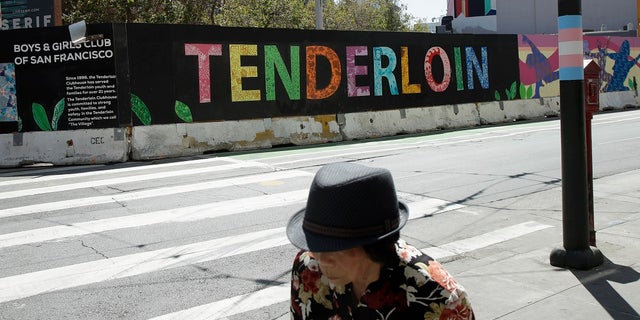 A person walks across the street from a sign for the Tenderloin neighborhood in San Francisco. (AP Photo/Jeff Chiu, File)