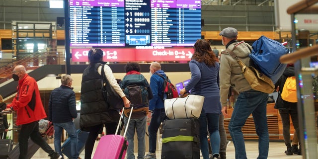 Travellers stand in front of an information board at BER Airport in Berlin, Germany, Saturday, Dec. 18, 2021. Germany’s incoming transport minister is advising people against traveling over Christmas as the country tries to stem a wave of coronavirus infections. (Joerg Carstensen/dpa via AP)