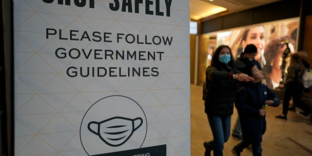 People walk past a sign outlining COVID-19 guidelines in the center of Amsterdam, the Netherlands, Saturday, Dec. 18, 2021. (AP Photo/Peter Dejong)
