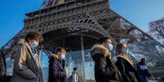 Des personnes portant des masques faciaux pour se protéger du COVID-19 passent devant la Tour Eiffel à Paris, le mardi 21 décembre 2021. (AP Photo/Michel Euler)