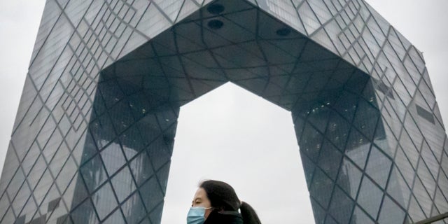 A woman wearing a face mask to protect against COVID-19 walks along a street in the central business district in Beijing, Thursday, Dec. 23, 2021. (AP Photo/Mark Schiefelbein)
