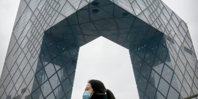 Una mujer que usa una mascarilla para protegerse del COVID-19 camina por una calle en el distrito comercial central de Beijing el jueves 23 de diciembre de 2021 (AP Photo / Mark Schiefelbein)