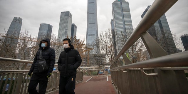 Los viajeros que llevan máscaras faciales para protegerse del COVID-19 cruzan una pasarela peatonal en el distrito comercial central de Beijing el jueves 23 de diciembre de 2021 (AP Photo / Mark Schiefelbein).