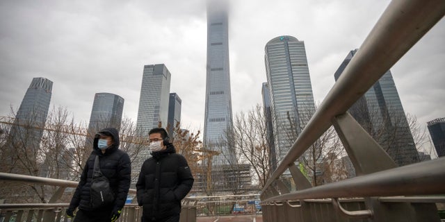 Commuters wearing face masks to protect against COVID-19 walk across a pedestrian bridge in the central business district in Beijing, Thursday, Dec. 23, 2021. (AP Photo/Mark Schiefelbein)