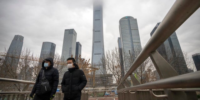 Los viajeros que llevan máscaras faciales para protegerse del COVID-19 cruzan una pasarela peatonal en el distrito comercial central de Beijing el jueves 23 de diciembre de 2021 (AP Photo / Mark Schiefelbein).