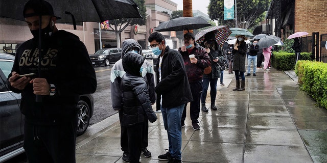 People stand in the rain as they wait in line for a COVID-19 test in Beverly Hills, California, Thursday, Dec. 23, 2021.