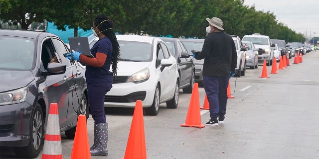 Employees of Nomi Health check in a long line of people for COVID-19 tests, Tuesday, Dec. 21, 2021, in North Miami, Florida.