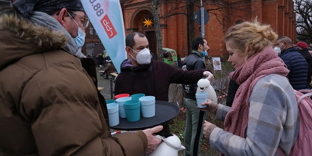 A volunteer distributes hot tea to people waiting in line to be inoculated against Covid-19 outside the Twelve Apostles Church on December 15, 2021 in Berlin, Germany. (Photo by Sean Gallup/Getty Images)