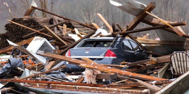 A car sits under a house destroyed by a tornado in Campbellsville, Ky