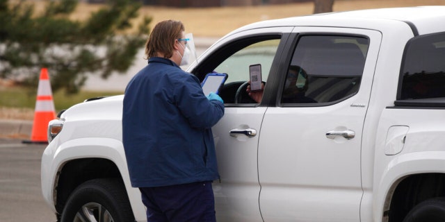 Um funcionário verifica a entrada de um cliente em uma estação de testes COVID-19 drive-up fora do centro de justiça quinta-feira, 9 de dezembro de 2021, em Castle Rock, Colorado.