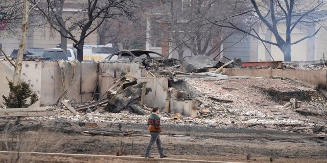 A man walks a foot path Friday near the remains of homes burned by wildfires after they ripped through a development in Superior, Colo.