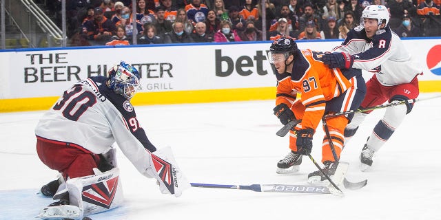 Columbus Blue Jackets goalie Elvis Merzlikins (90) makes a save against Edmonton Oilers' Connor McDavid (97) as Blue Jackets' Zach Werenski (8) defends during second-period NHL hockey game action in Edmonton, Alberta, Thursday, Dec. 16, 2021.