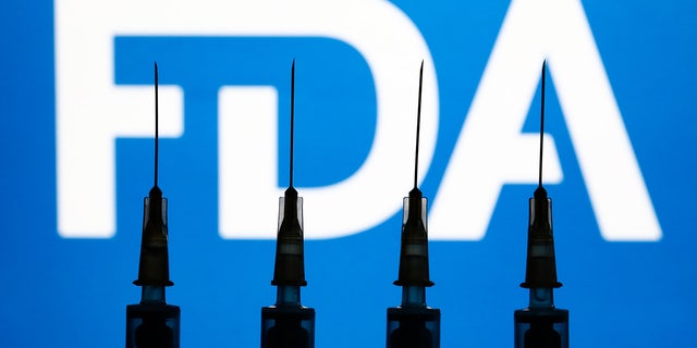 Medical syringes and FDA logo displayed in the background are seen in this illustration photo taken in Krakow, Poland on Dec. 2, 2021.