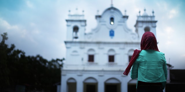 Young Christian woman standing in front of a church in Goa, India. (rvimages via Getty Images)