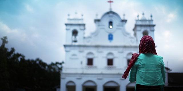 Young Christian woman standing in front of a church in Goa, India. (rvimages via Getty Images)