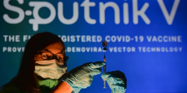 A person holding a medical syringe and a vaccine vial in front of the Sputnik V logo displayed on a screen. Op Donderdag, Oktober 21, 2021, in Edmonton, Alberta, Kanada. 
