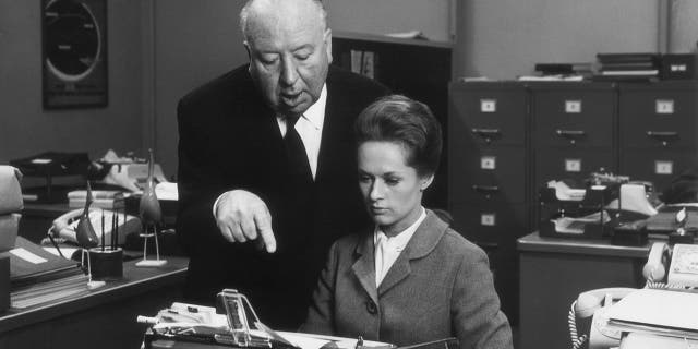 British director Alfred Hitchcock directs American actress Tippi Hedren while she sits in front of a typewriter on the set of his film "Marnie."