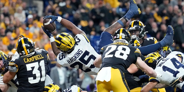Michigan running back Hassan Haskins (25) scores on a 1-yard touchdown run ahead of Iowa linebacker Jack Campbell (31) during the second half of the Big Ten championship NCAA college football game, Saturday, Dec. 4, 2021, in Indianapolis.