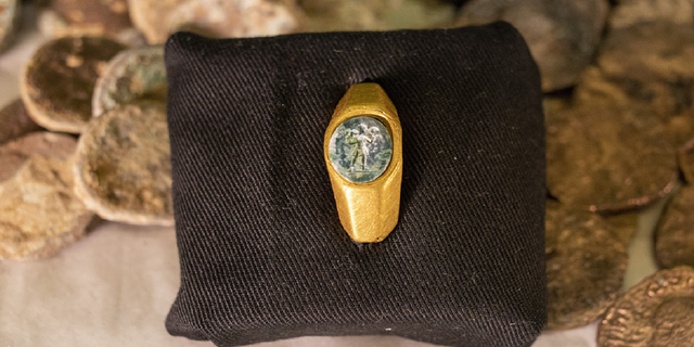 A Roman gold ring, its green gemstone carved with the figure of a shepherd carrying a sheep on his shoulders, is on display with coins that where found near the ancient city of Caesarea, dated to the Roman and Mamluk periods, around 1,700 and 600 years ago, in Jerusalem on Wednesday.