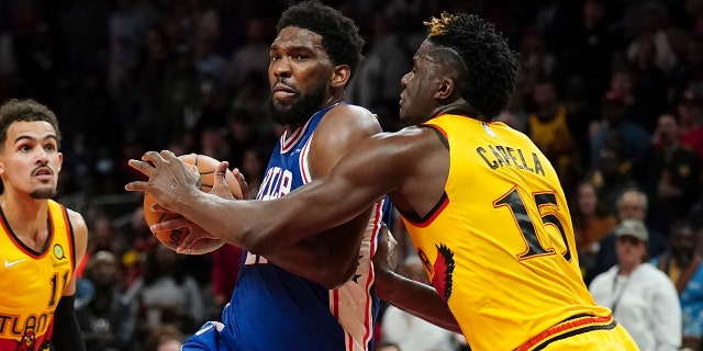 Philadelphia 76ers center Joel Embiid, center, tries to drive past Atlanta Hawks center Clint Capela (15) Friday, Dec. 3, 2021, in Atlanta.