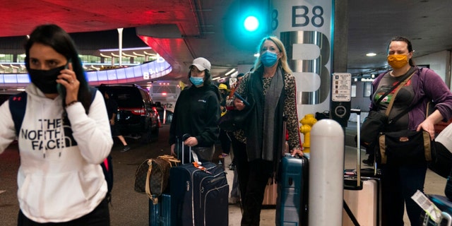 Travelers wearing protective face masks wait for a shuttle to arrive at the Los Angeles International Airport Tuesday, Nov. 30, 2021. (AP Photo/Jae C. Hong) 