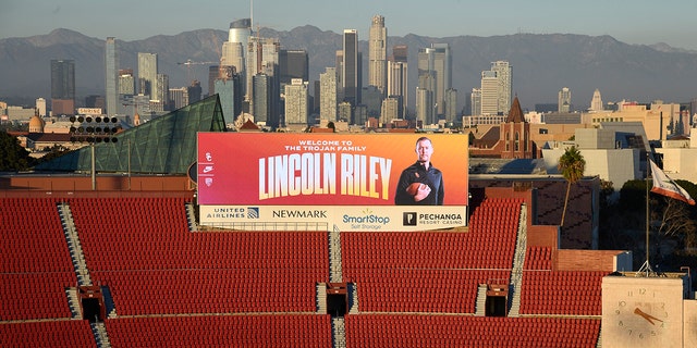 A large billboard at the Los Angeles Coliseum displays a photo of new USC football coach Lincoln Riley with downtown Los Angeles as a backdrop.