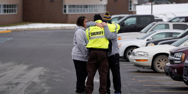 An Oakland County Sheriff's deputy hugs family members of a student in the parking lot of Oxford High School in Oxford, Mich., Wednesday, Dec. 1, 2021. A 15-year-old sophomore opened fire at the school, killing several students and wounding multiple other people, including a teacher. (AP Photo/Paul Sancya)
