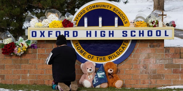 A well wisher kneels to pray at a memorial on the sign of Oxford High School in Oxford, Mich.,   on Wednesday, Dec. 1, 2021. A 15-year-old sophomore opened fire at the school, killing several students and wounding multiple other people, including a teacher. 