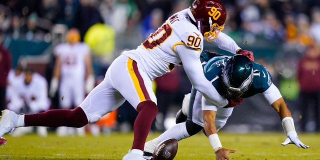 Philadelphia Eagles quarterback Jalen Hurts, right, fumbles the ball as he is hit by Washington Football Team's Montez Sweat during the first half of an NFL football game, Tuesday, Dec. 21, 2021, in Philadelphia.