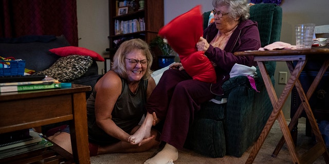 Susan Ryder, 54, giggles as she applies an ointment to the base of her mother's foot before bedtime, Monday, Nov. 29, 2021, in Rotterdam Junction, New York.