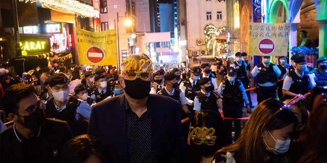 A man wearing festive glasses stands in front of police at Hong Kong's Lan Kwai Fong area on Jan. 1, 2022.