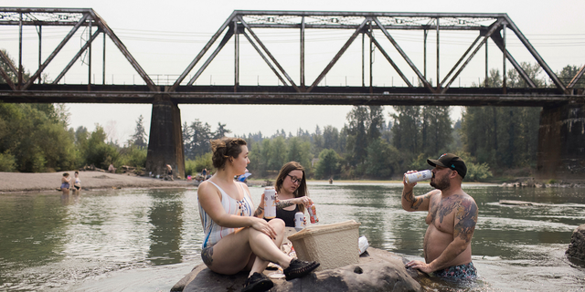 Mirian Perala, Addie Cold and Joe St. Martin enjoy lunch on a rock in the middle of the Sandy River near Troutdale, Oregon, Aug.13 during a heat wave. 