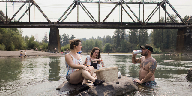 Mirian Perala, Addie Cold and Joe St. Martin enjoy lunch on a rock in the middle of the Sandy River near Troutdale, Oregon, Aug.13 during a heat wave. 