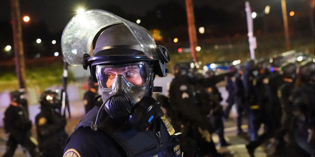 ​​​​​​​A Portland, Ore., police officer scans the crowd while dispersing protesters, Aug. 21, 2020. 
