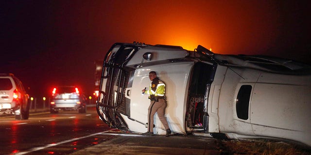 An Iowa State Patrol trooper works the scene of an overturned semi-truck along the westbound shoulder of Interstate 80 near Anita, Iowa, after a band of intense weather crossed through the area. 
