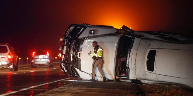 An Iowa State Patrol trooper works the scene of an overturned semi-truck along the westbound shoulder of Interstate 80 near Anita, Iowa, after a band of intense weather crossed through the area.