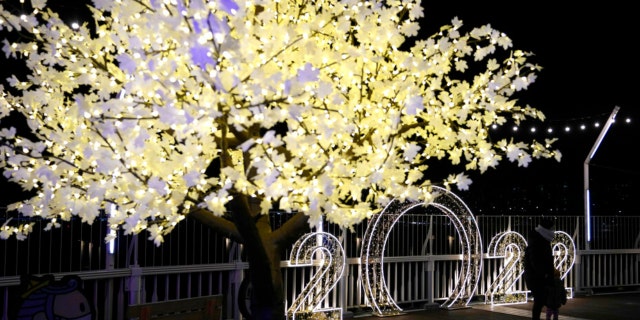A visitor wearing a face mask pose for a photo in front of illuminated decorations on New Year’s Eve in Seoul, South Korea, Friday, Dec. 31, 2021.