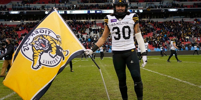 12 월 5, 2021; 토론토, 온타리오, 할 수있다; Hamilton Tiger-Cats defensive back Stavros Katsantonis (30) poses with a team flag on the field after a win over the Toronto Argonauts in the Canadian Football League Eastern Conference Final game at BMO Field.