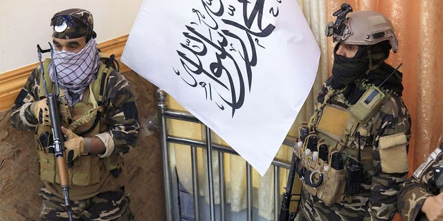 Taliban fighters stand guard next to a Taliban flag during a gathering where Afghan Hazara elders pledged their support to the country's new Taliban rulers, in Kabul on November 25, 2021. 