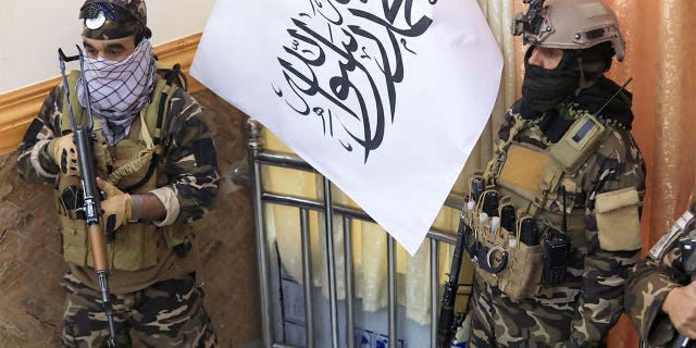 Taliban fighters stand guard next to a Taliban flag during a gathering where Afghan Hazara elders pledged their support to the country's new Taliban rulers, in Kabul on November 25, 2021.